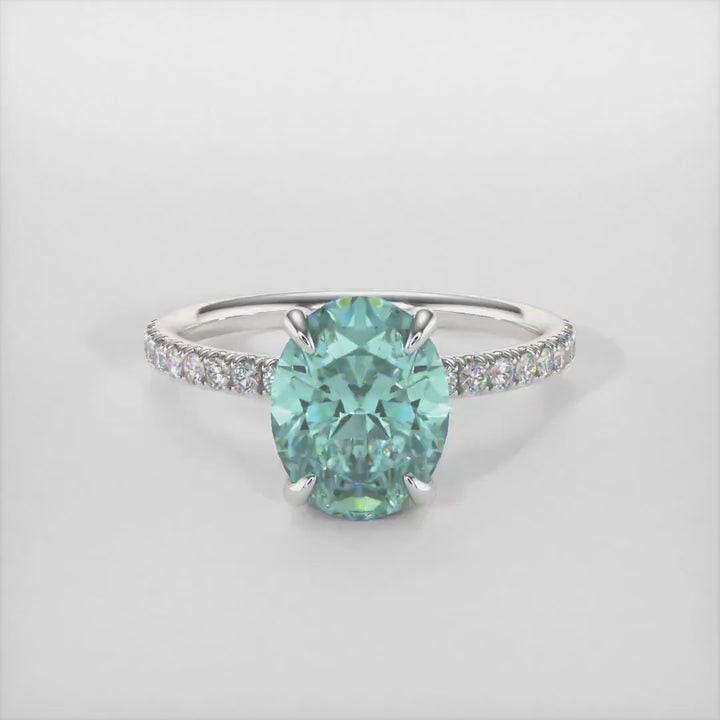Abigail Oval Aqua Teal Moissanite Engagement Ring/ AGI Design. A beautiful engagement ring in gold or platinum that includes an Aqua-Teal Oval Moissanite set into the 4 prongs hidden halo setting. The band and the halo are covered with lab-created diamonds. This solitaire ring is designed to allow the wedding band to sit  flush with the engagement ring because the center stone sits directly above the band.