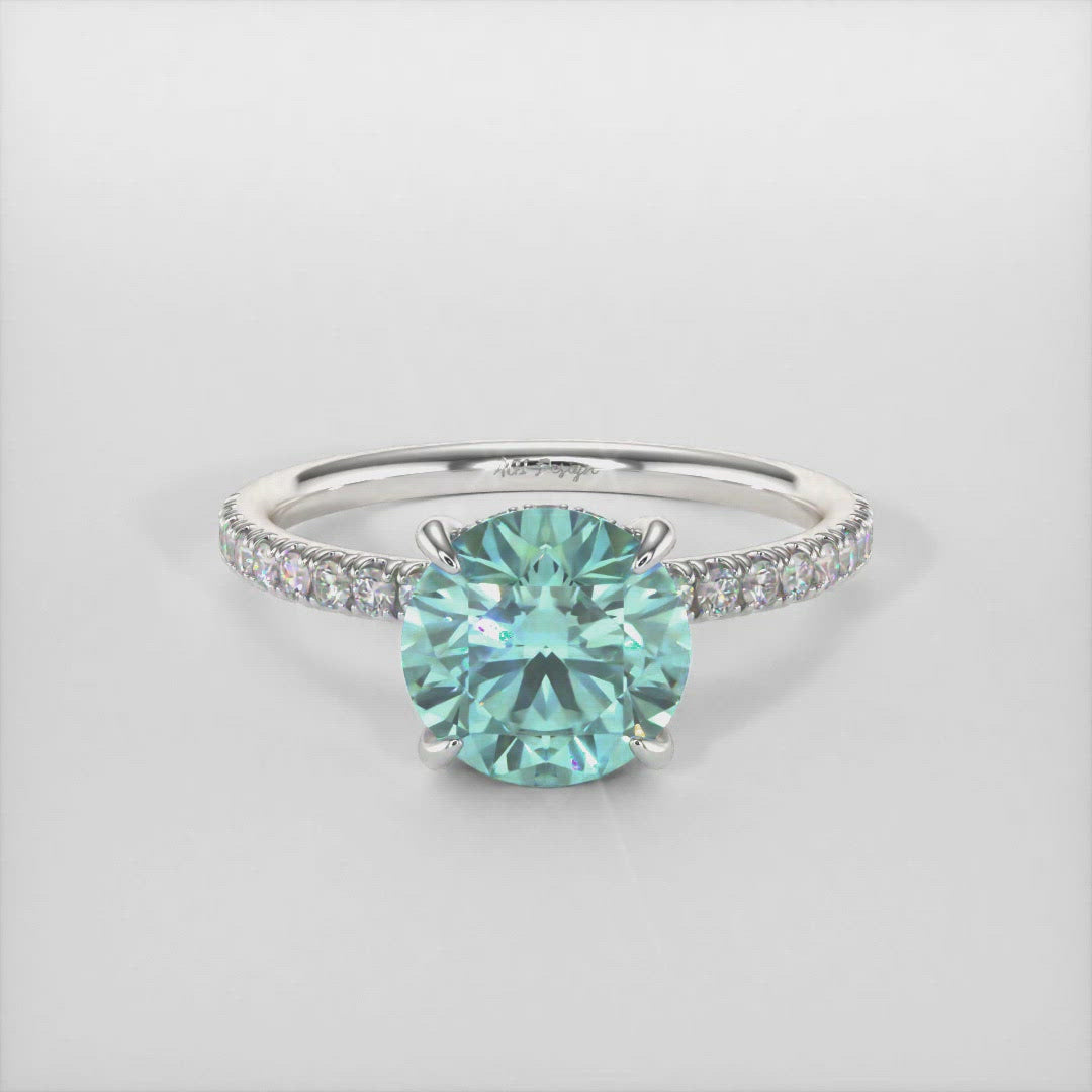 This incredible engagement ring features a round Aqua-teal Moissanite surrounded by a hidden halo of round Lab-Created brilliant-cut diamonds that make their way down the ring’s shank. This ring is designed to allow the wedding band to sit close and flush with the engagement ring. AGI Design