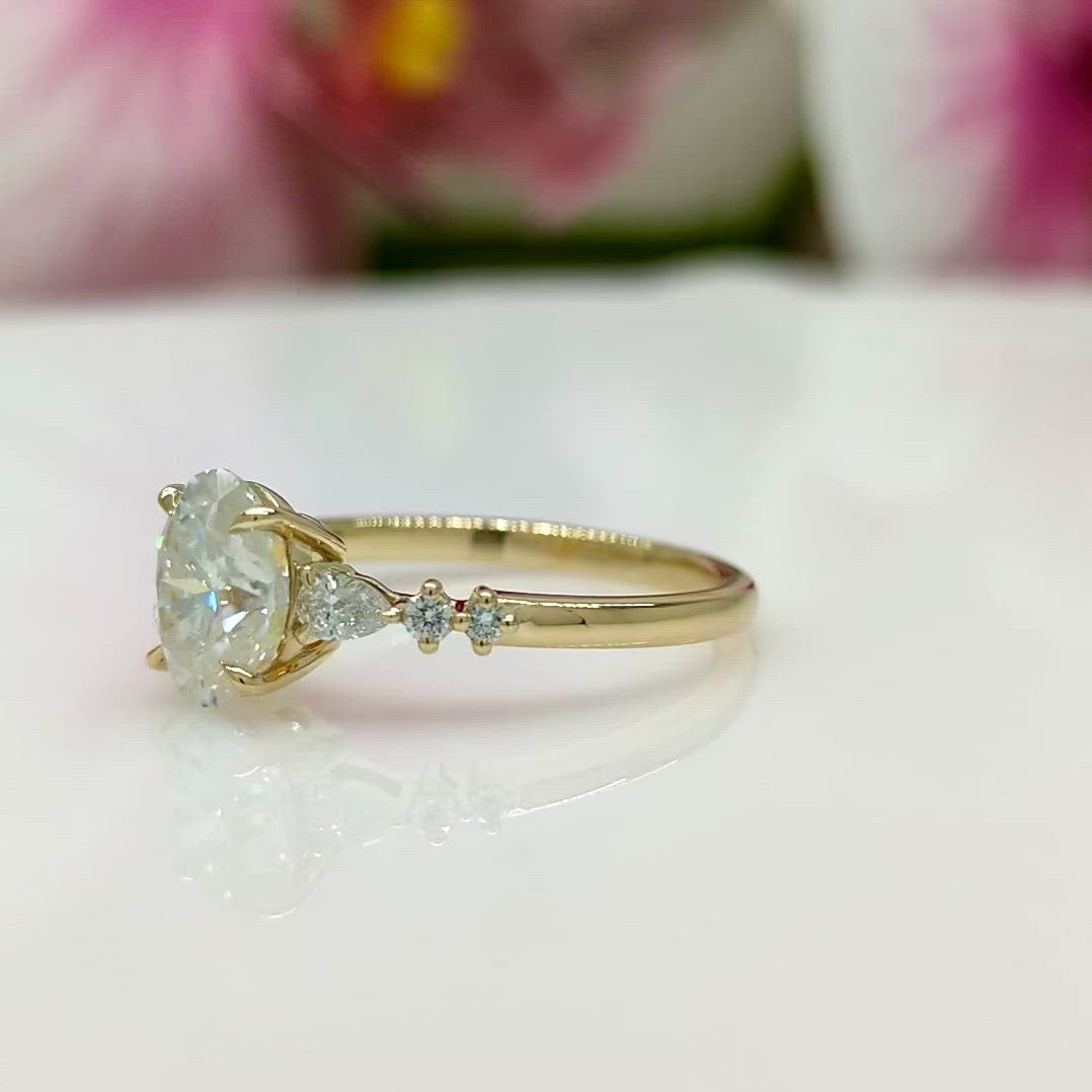 Emma Oval Moissanite Engagement Ring-AGI Design/In this lovely engagement ring in gold or platinum, you will find a 2ct colorless moissanite stone in an oval shape and two small pear-shaped lab-created diamonds on the side.